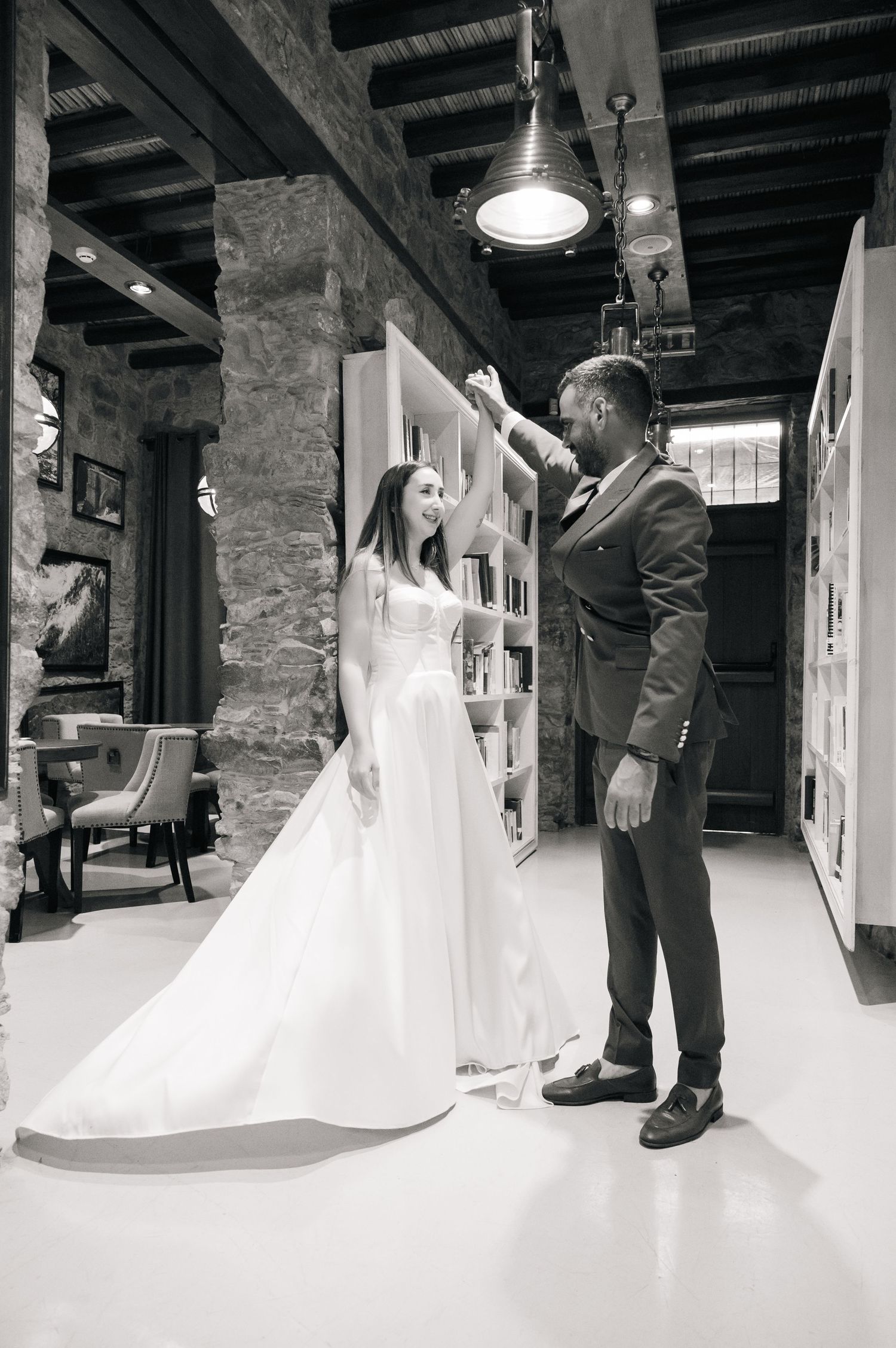 A couple dancing in a rustic indoor venue with exposed stone walls and pendant lighting.
