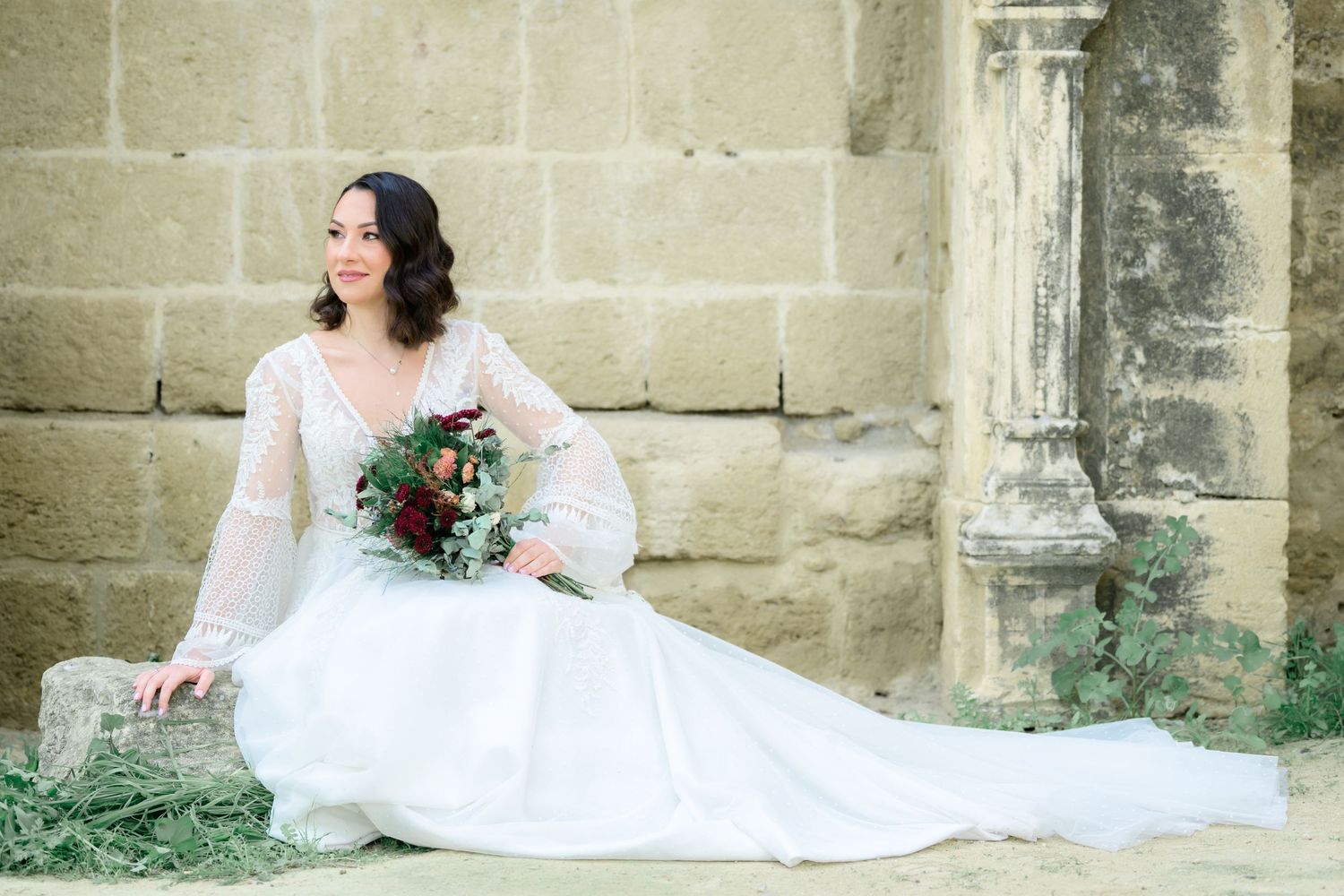 A white wedding dress elegantly flows across stone steps and pillars in an architectural setting.