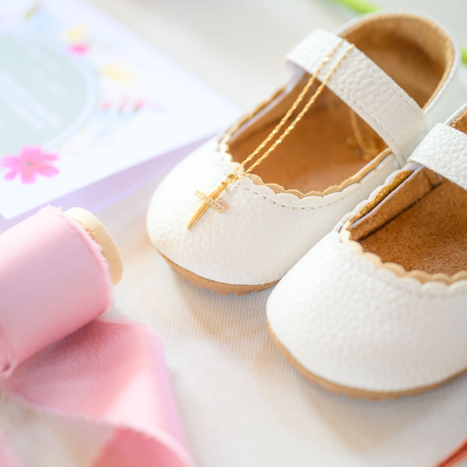 Delicate white leather baby Mary Jane shoes with pink macarons as decoration against a soft floral background.