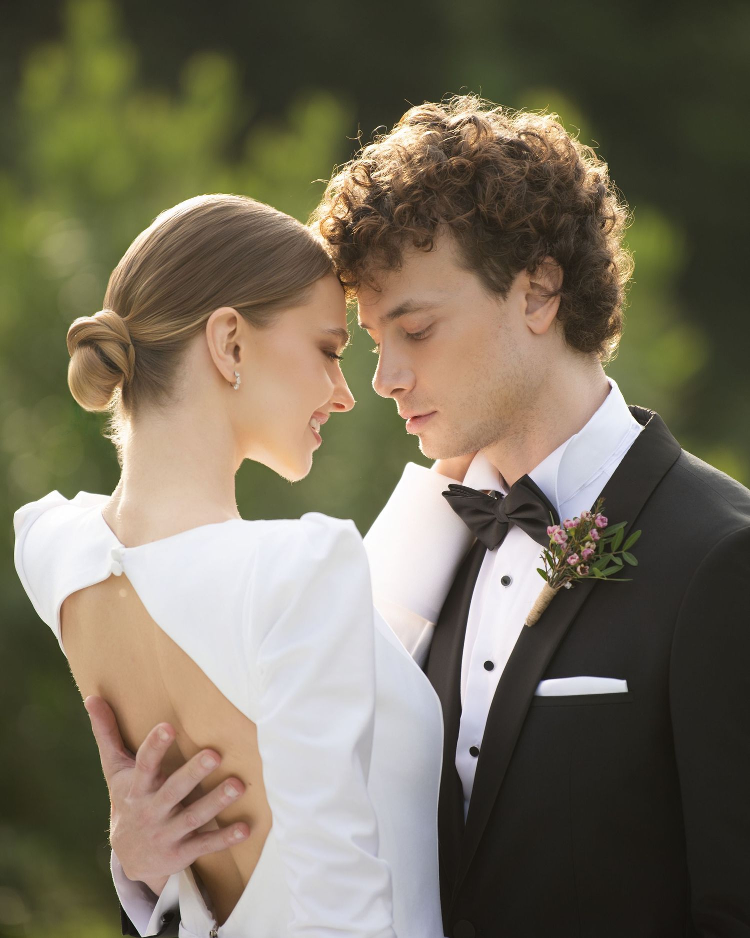 A romantic wedding portrait of a couple in formal attire sharing an intimate moment outdoors with soft natural lighting.