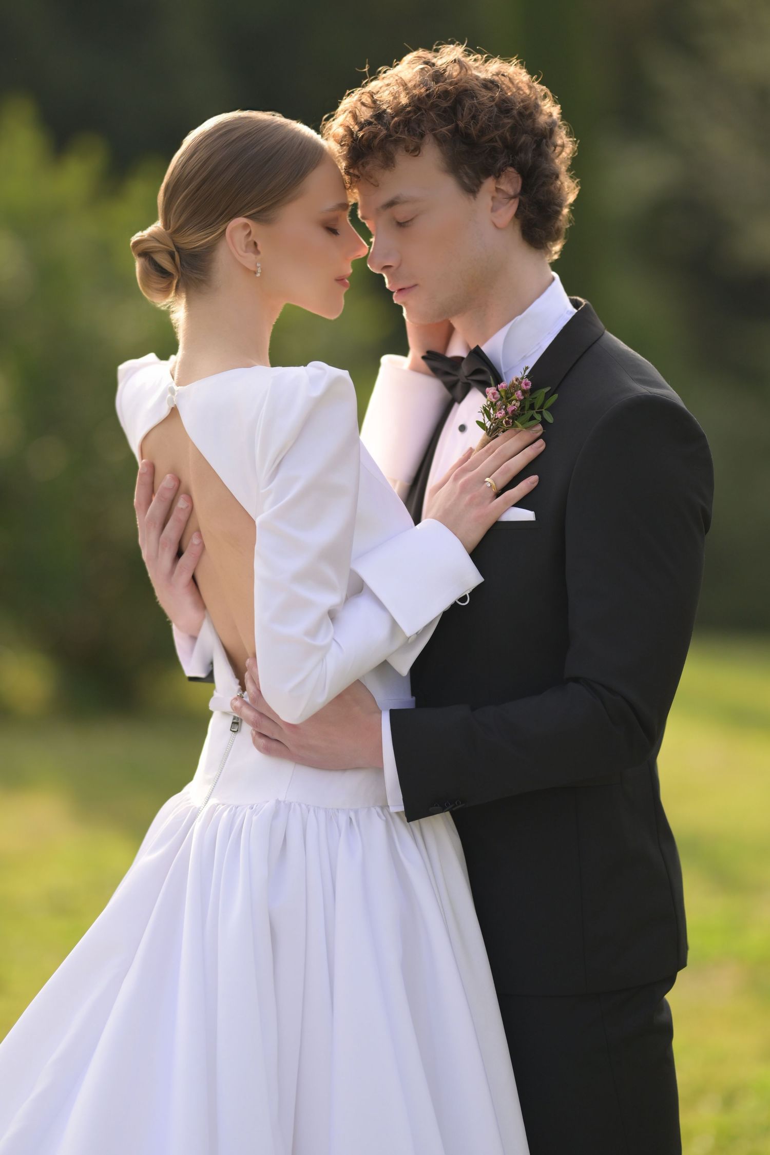 A romantic wedding couple in white dress and black suit embrace in a series of intimate poses in a sunlit garden.