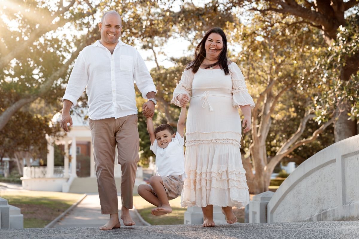 A family in white and beige outfits walks together during a golden sunset photoshoot at an outdoor location in balmoral beach mosman