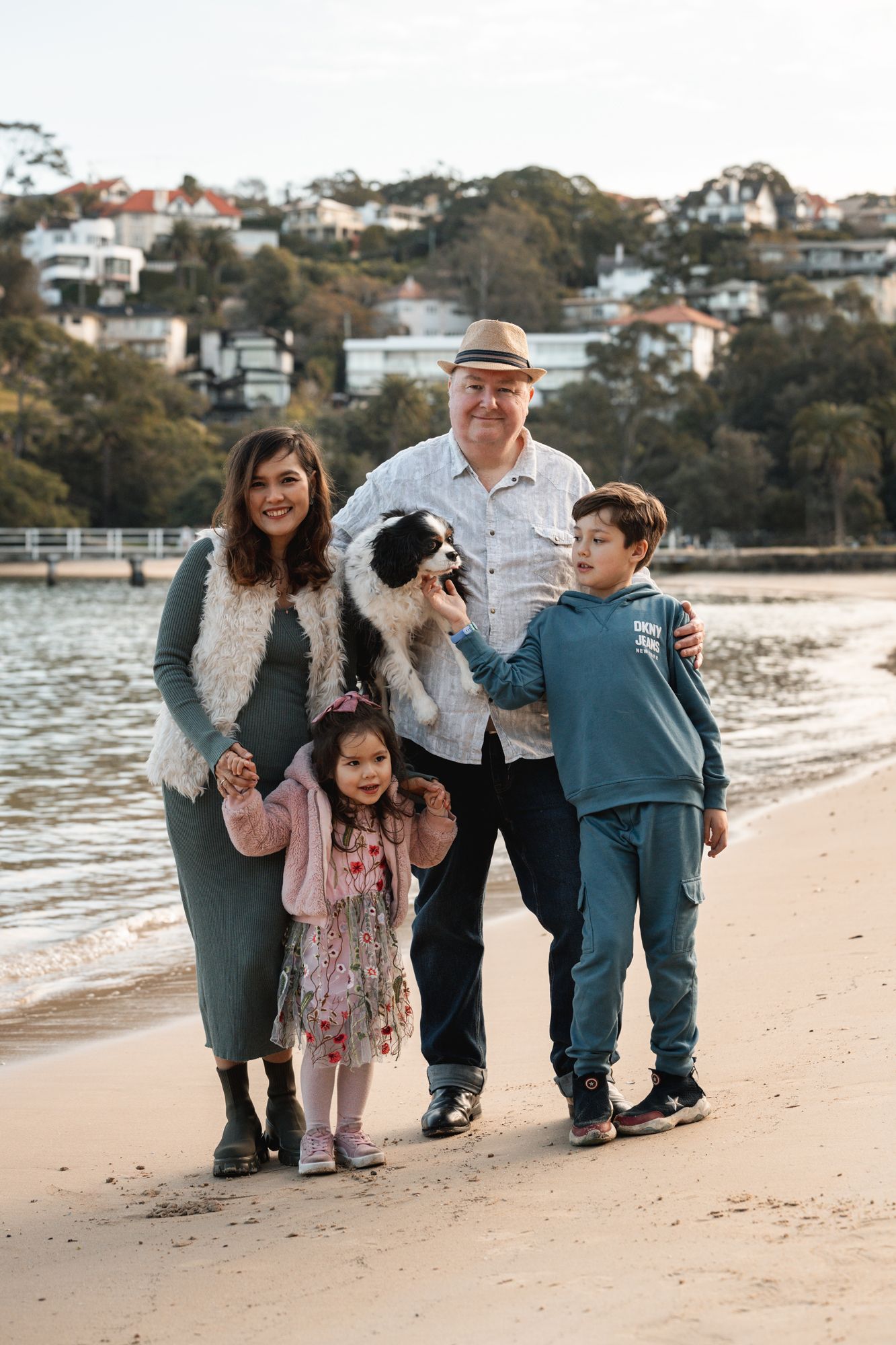 Family and dog enjoying a sunset stroll along a sandy beach with waterfront homes visible on the hillside in the background Clifton gardens