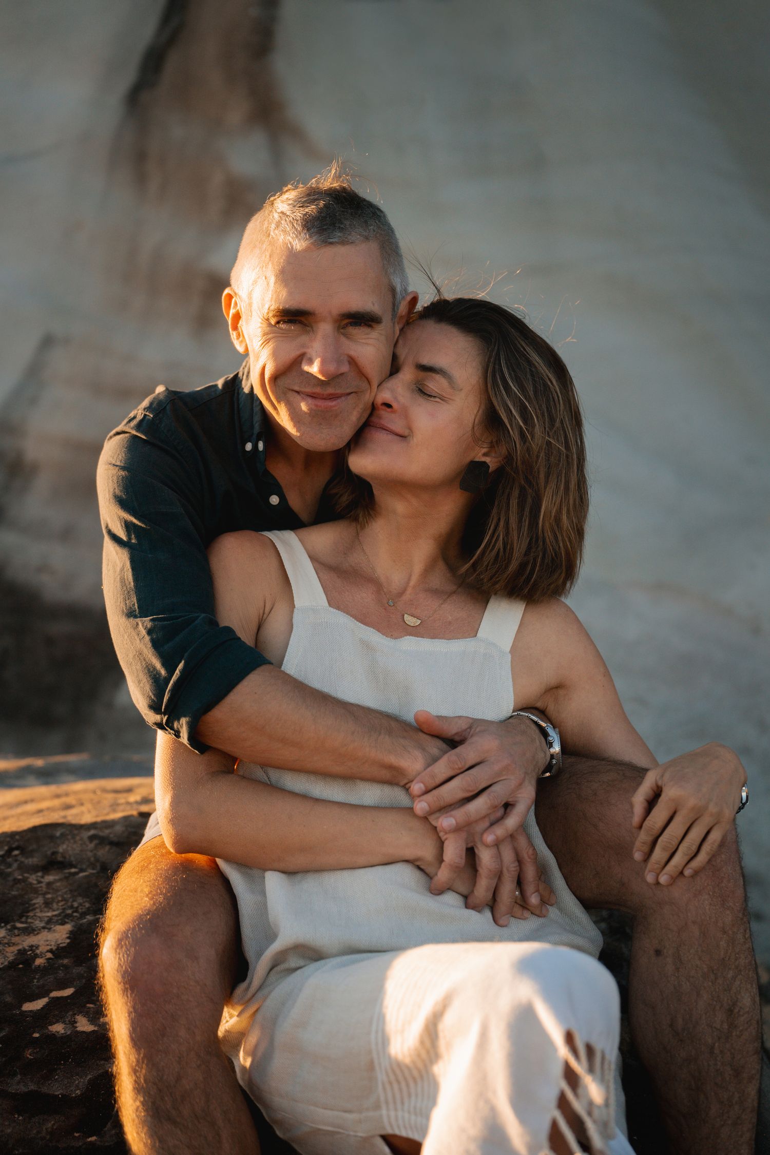 A romantic couple embraces on a rocky beach at sunset, creating an intimate moment in golden light during a couples photoshoot in Sydney