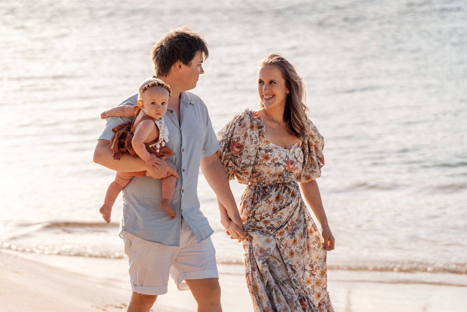 A couple walks along the beach at sunset in floral dress and casual attire while sharing intimate moments together.