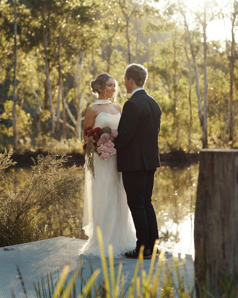 Bride and groom share a romantic moment on a dock surrounded by lush Australian bushland and a tranquil river during an elopement photoshoot