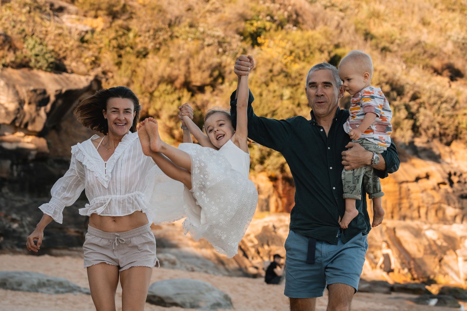 a family is playful during a family phototoshoot in North Curl Curl Northern Beaches Sydney in sunset with golden cliffs in the background.