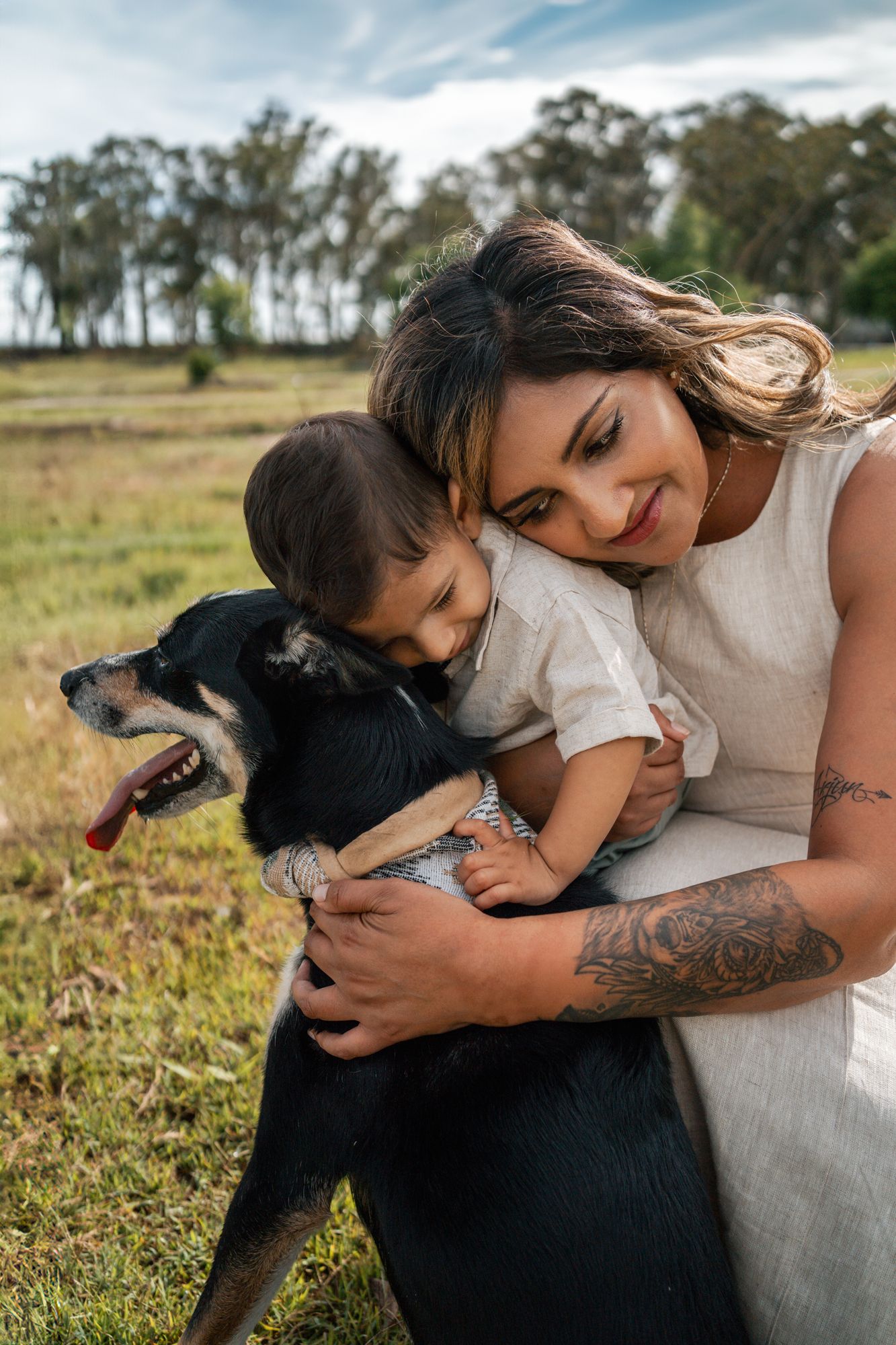 A tender moment between a mom a one year old and their black dog in a sunny outdoor field during a family photoshoot with a dog in Rouse Hil