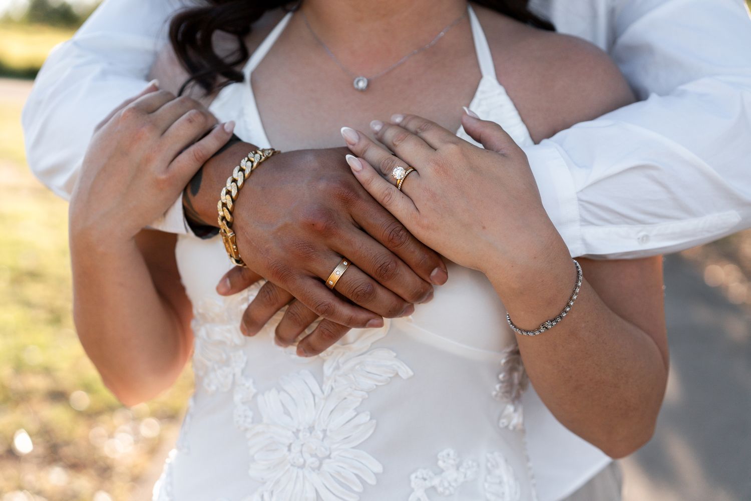 A person in a white wedding dress holds a bouquet while another person in a suit stands nearby during an outdoor ceremony.