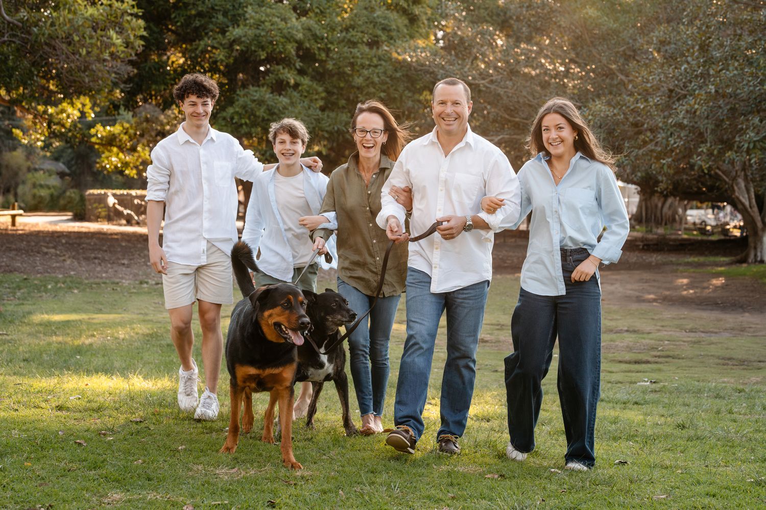 A family wearing coordinated denim outfits poses together outdoors during a golden sunset family photoshoot with their dog in Sydney