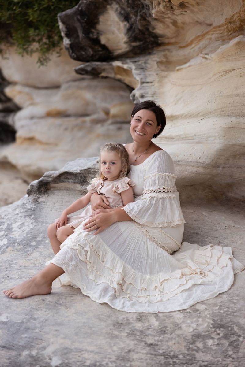 Mum and daughter sitting together on a rocky outcrop against a textured sandstone wall during family photoshoot in balmoral beach sydney