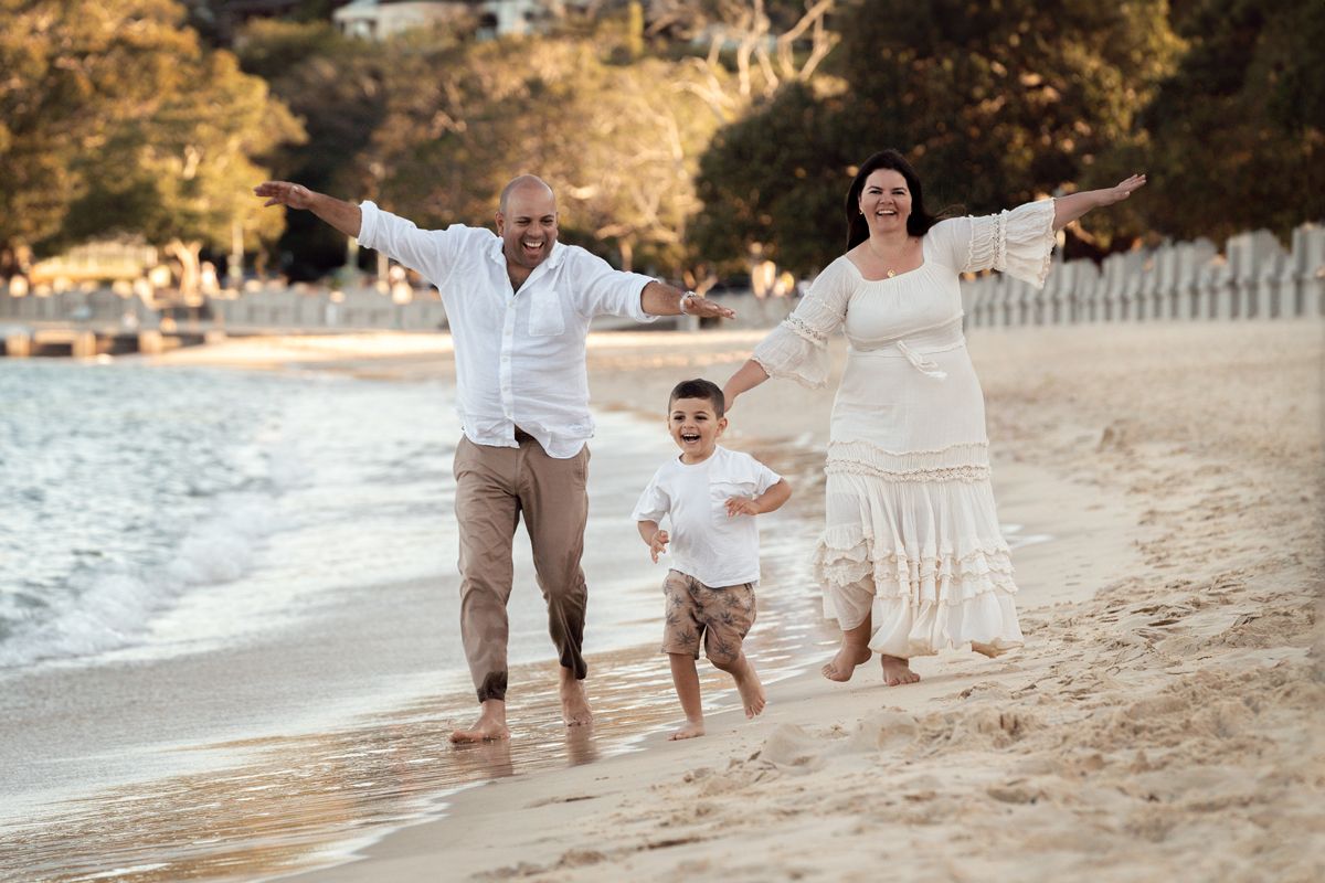 A family wearing white clothing walks together along a sandy beach at sunset photoshoot in sydney balmoral beach