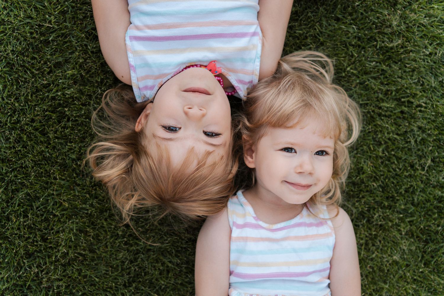 girl siblings lying on green grass in a striped shirt, taken from above during a family photoshoot in Rouse hill Sydney Hills district