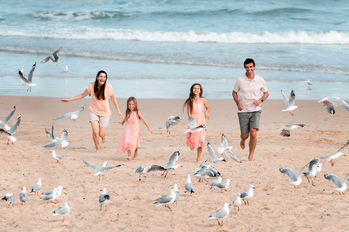 People walking on a sandy beach with seagulls flying around them as waves roll in from the ocean.