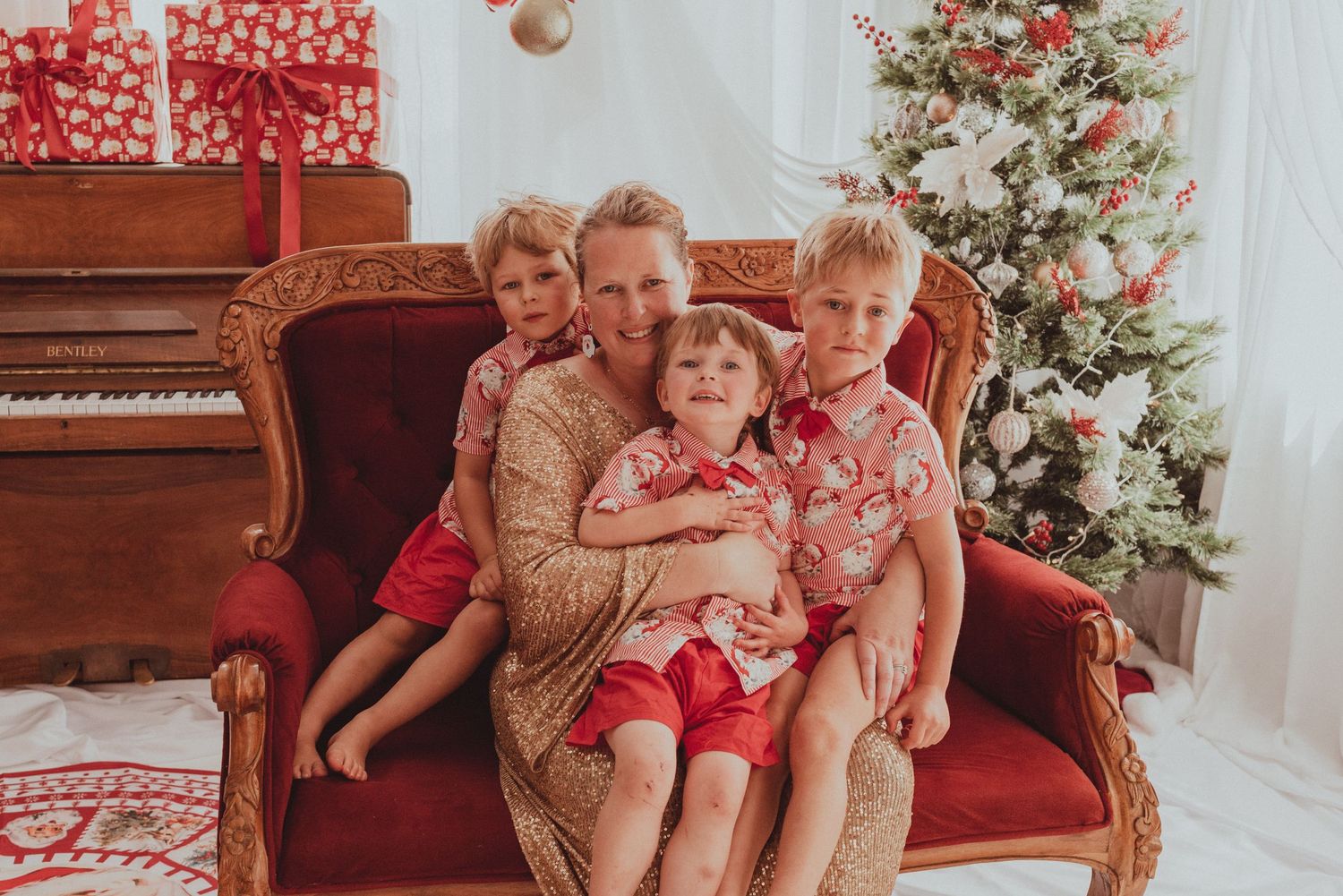 Family sitting together on vintage red couch during Christmas with piano and decorated tree.