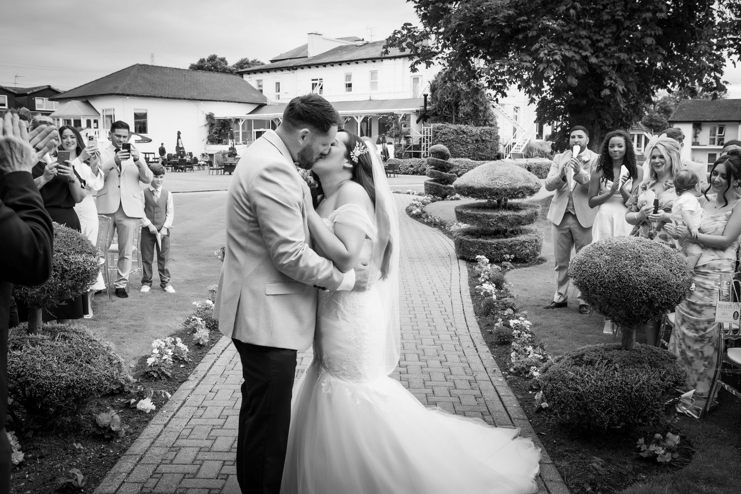The wedding couple is shareing a romantic kiss during the wedding ceremony in the Thornton Hall garden with surrounded by family and friends