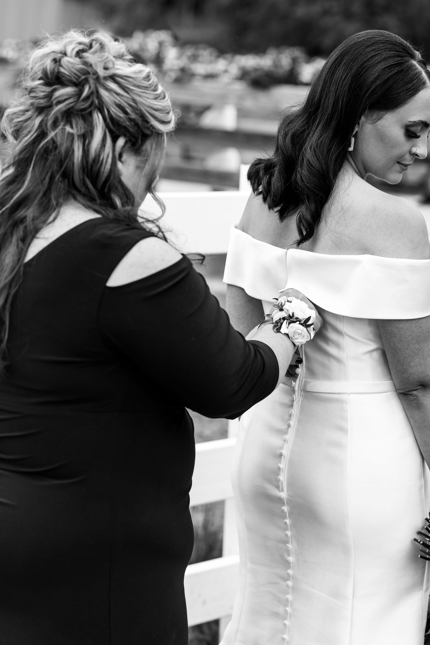 Black and white photo of bridal dress being buttoned up during wedding preparations.