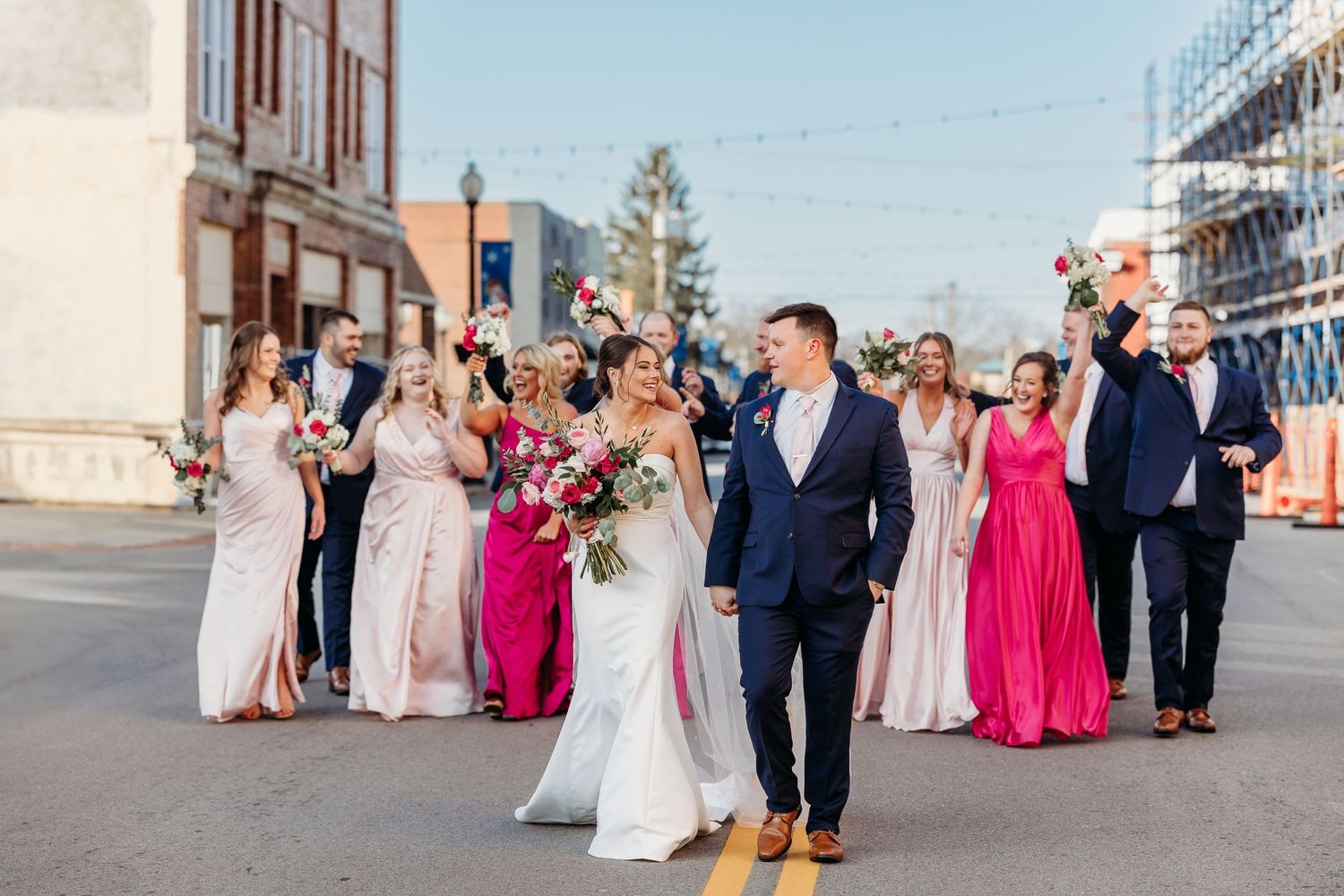 Wedding party walking down city street with bridesmaids in pink dresses.