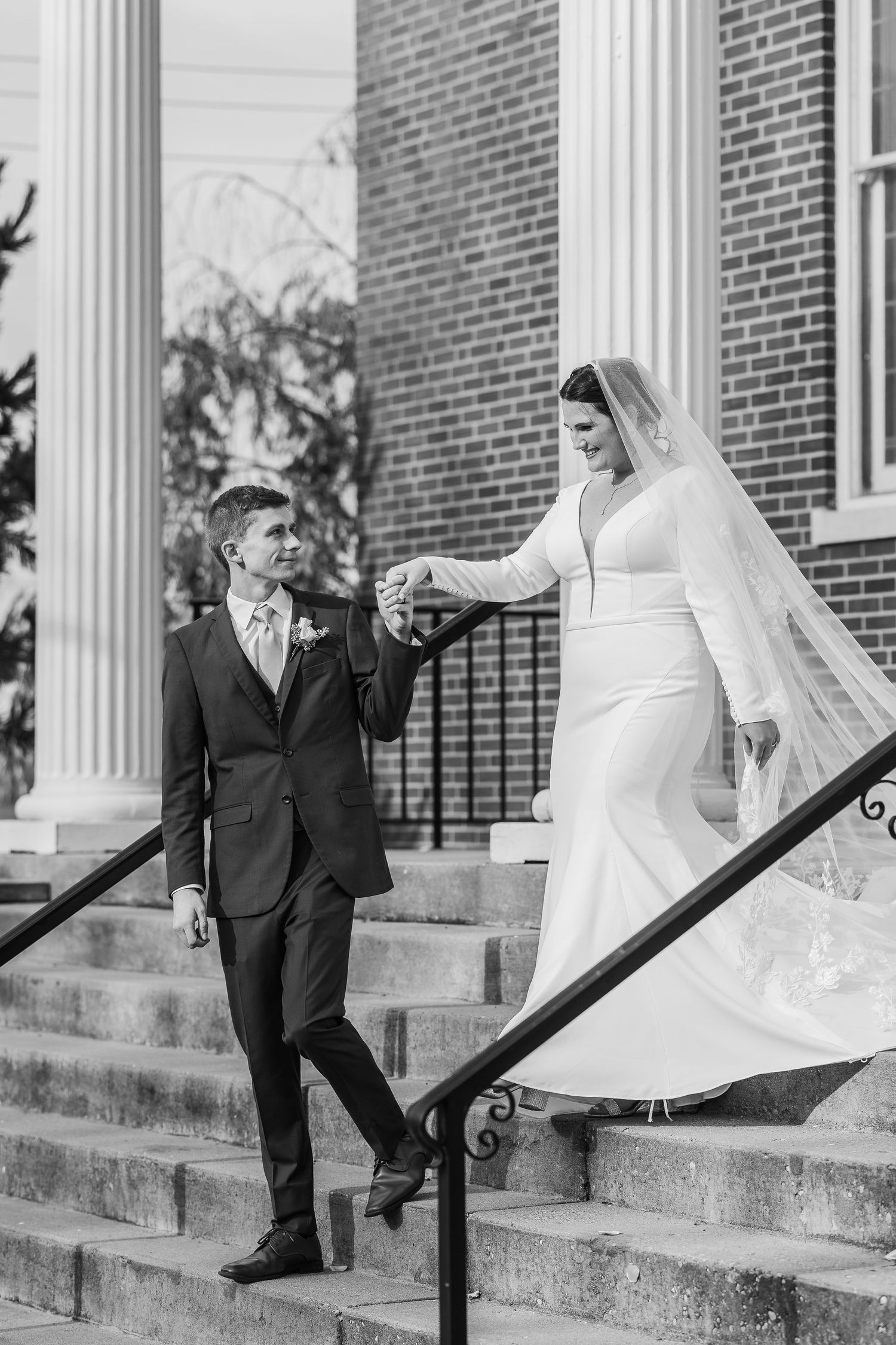 Classic black and white wedding photo of couple descending church steps with elegant columns.