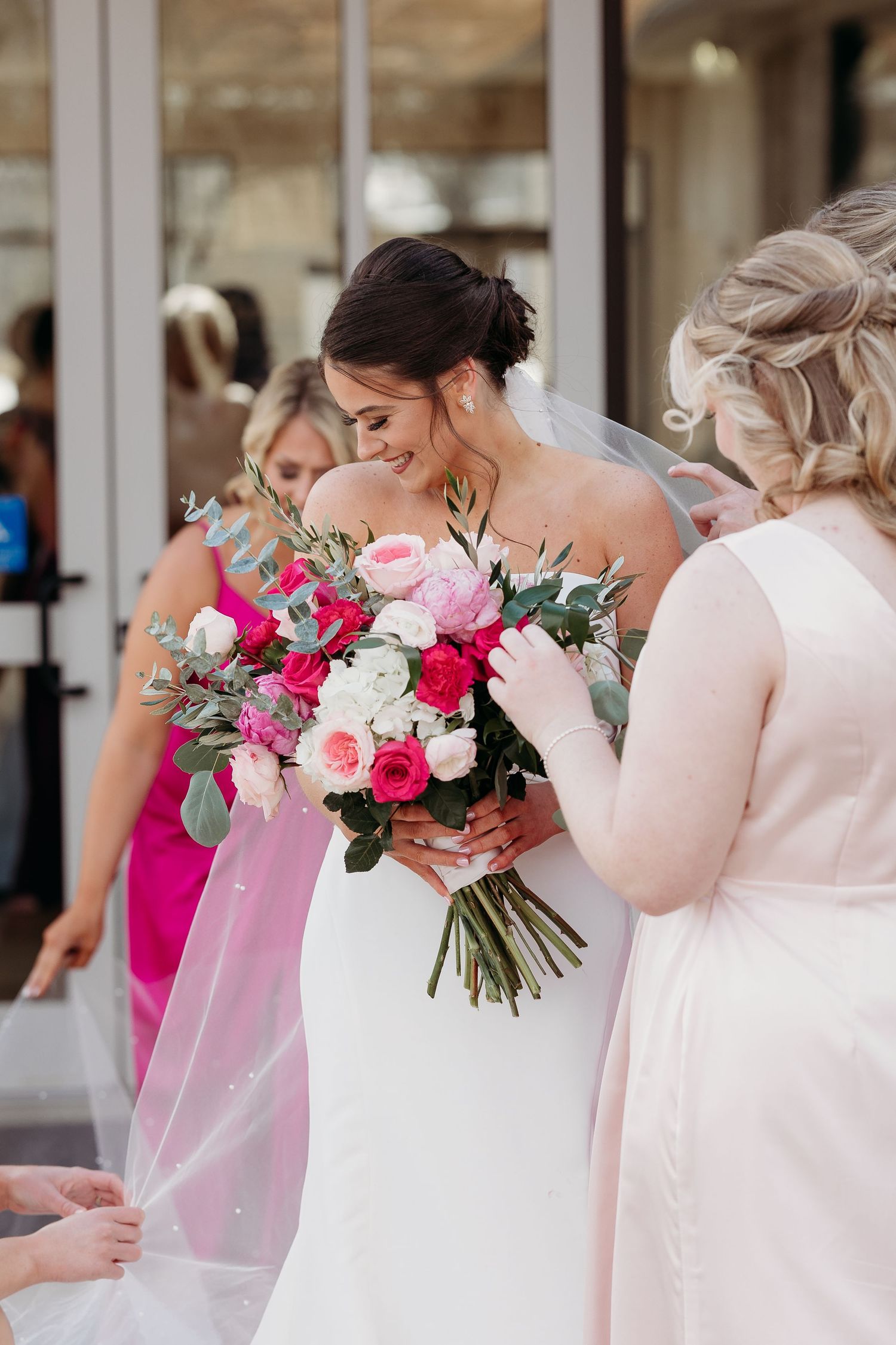 Bride holds vibrant pink and white wedding bouquet while surrounded by bridesmaids in blush dresses.