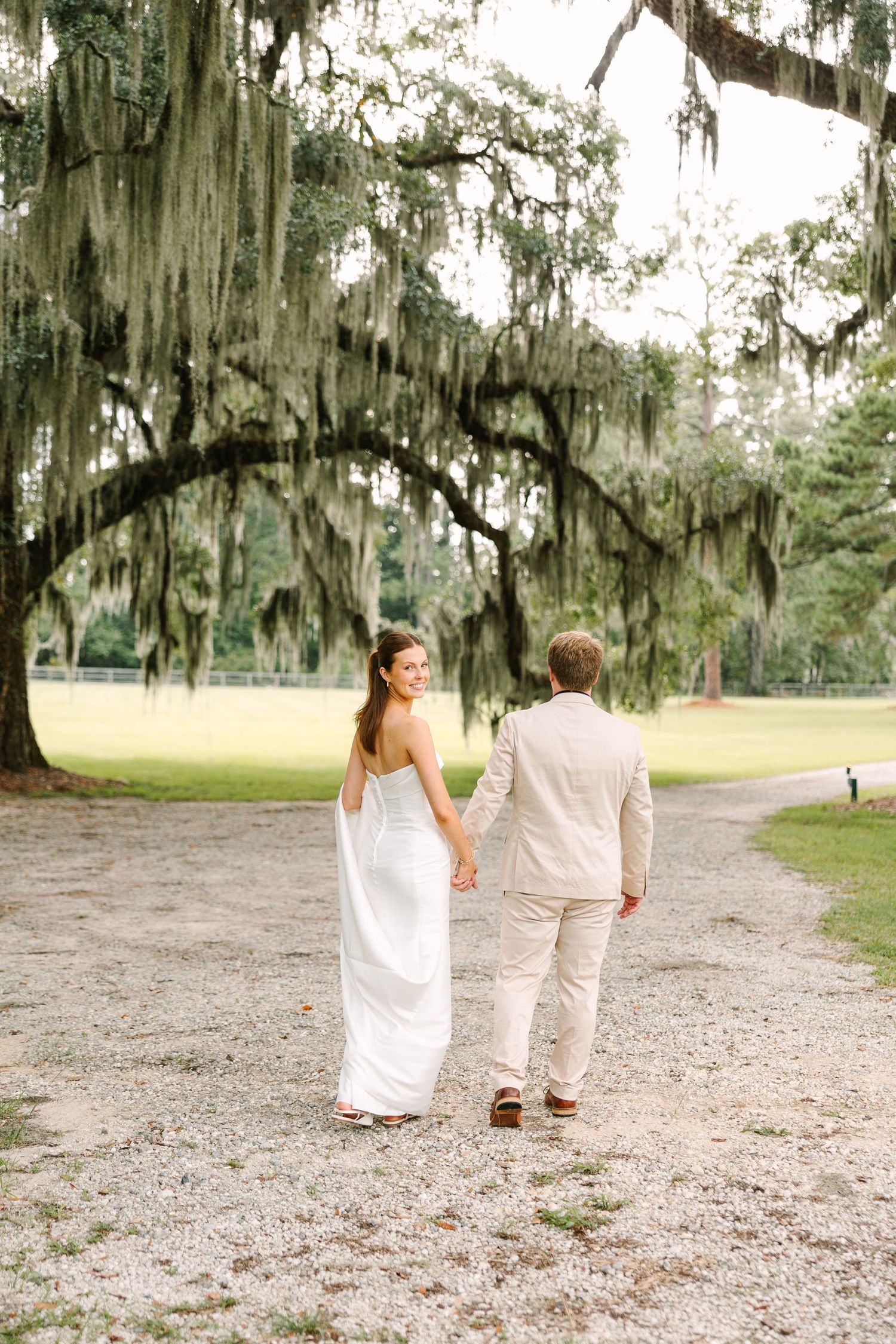 A romantic walk under Spanish moss-draped trees in elegant wedding attire.