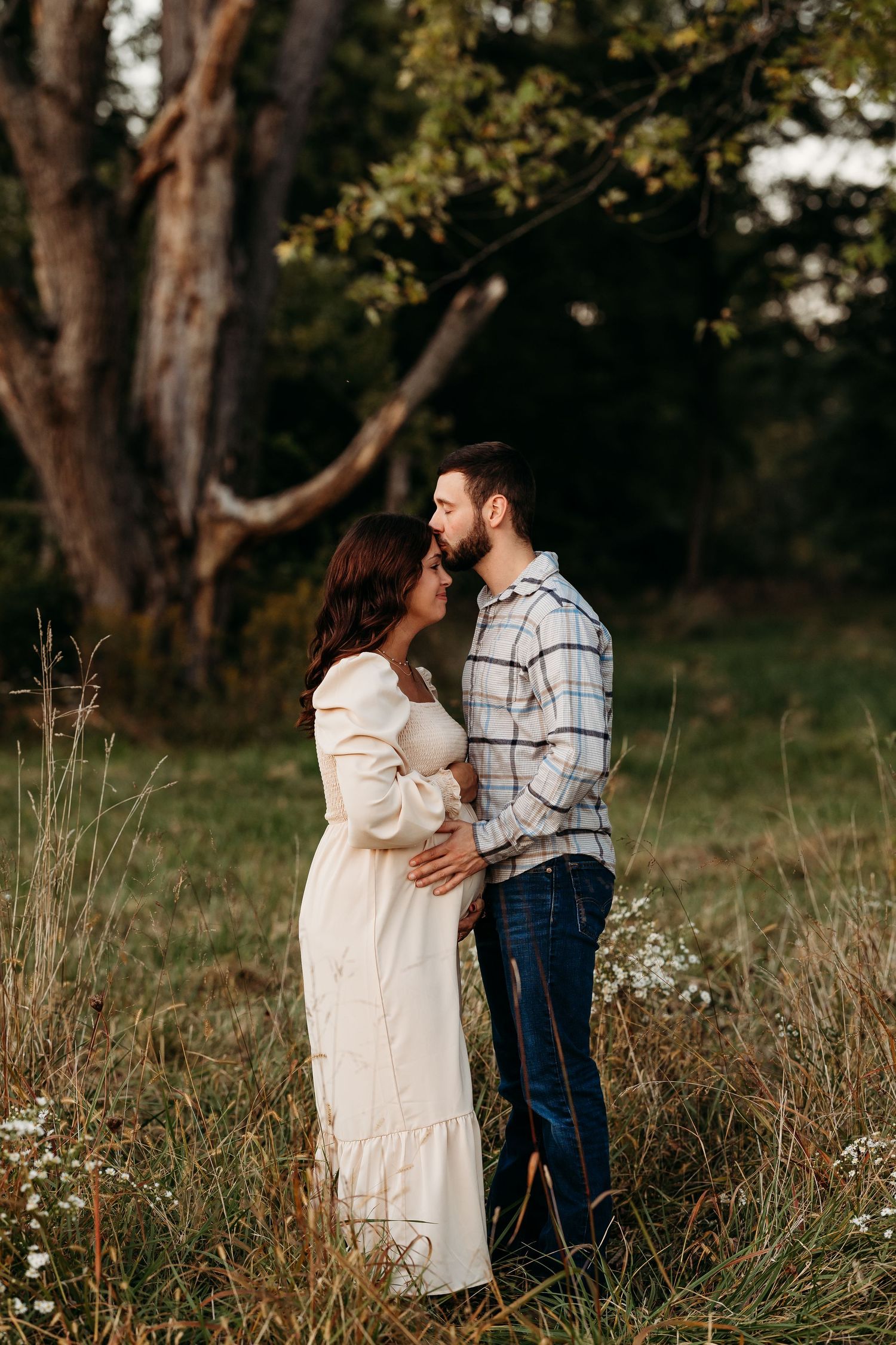 Couple in casual attire embracing in a golden field at sunset.