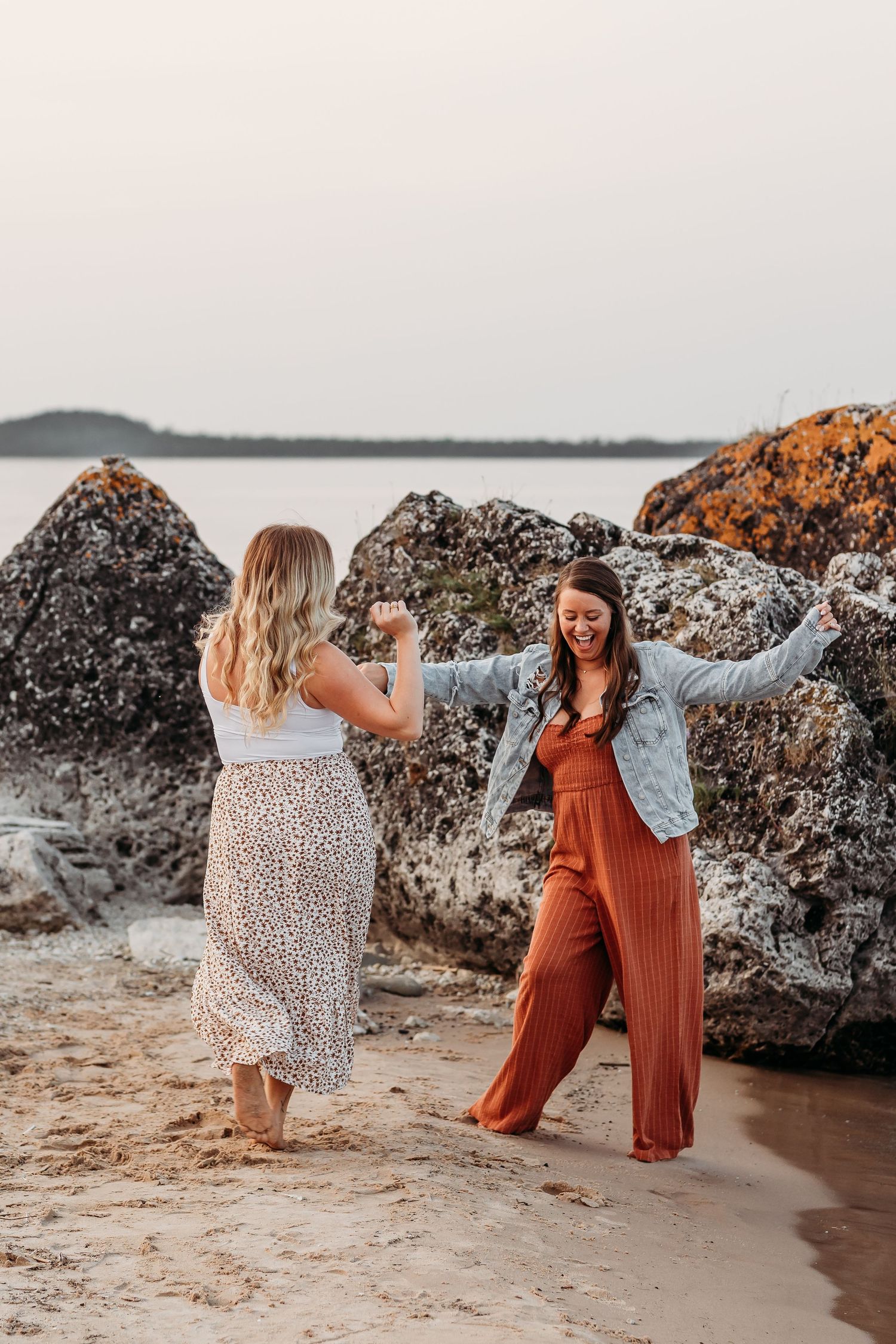 Friends dancing and laughing together on a rocky beach at sunset.