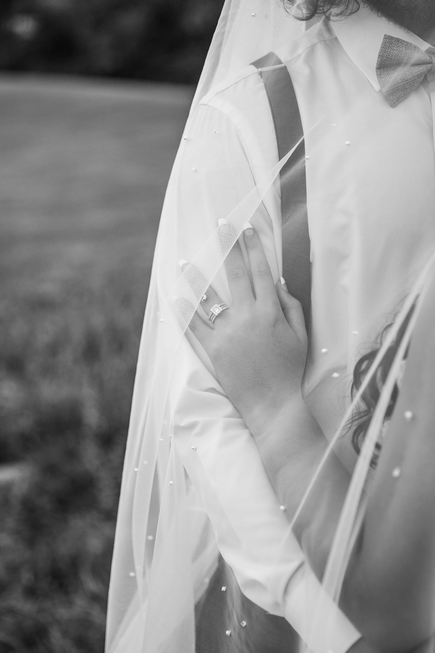 Close-up detail of a white wedding dress veil and sleeve against a blurred outdoor background.
