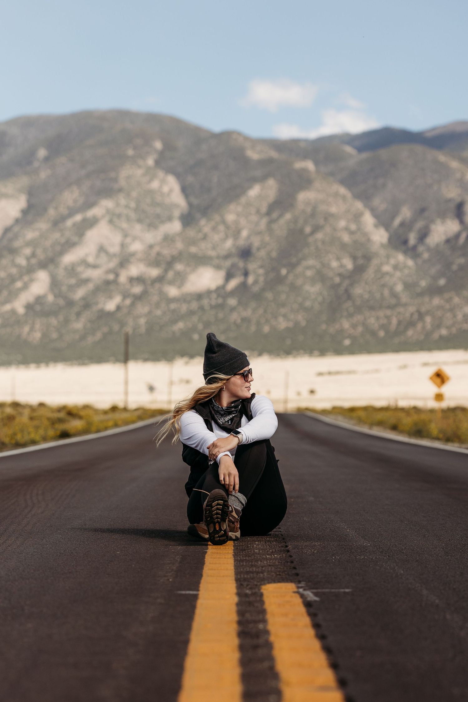 Person in winter clothing sitting in middle of empty mountain highway.