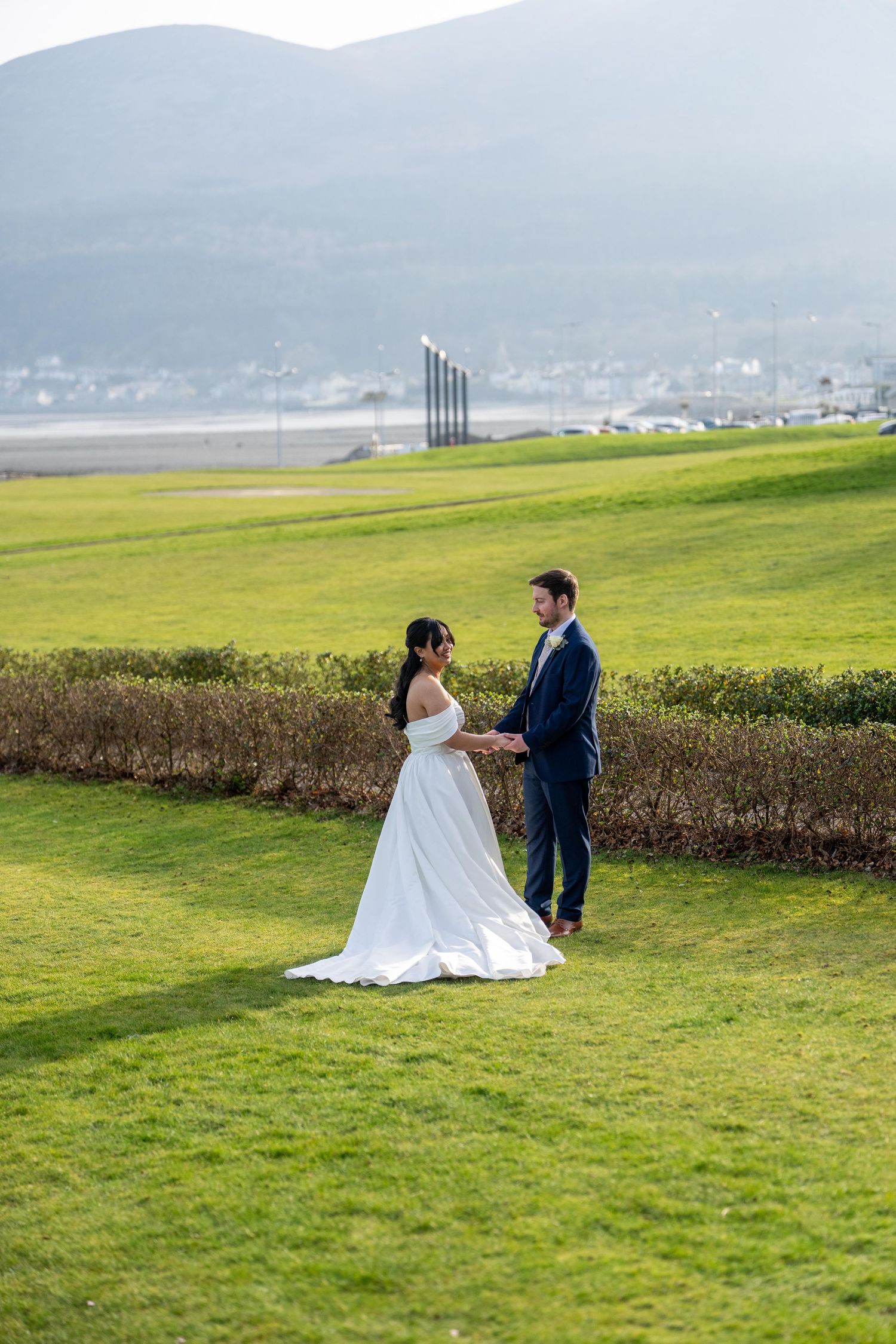 Bride and groom hold hands Slieve Donard with mountain and coastal backdrop on their wedding day. Dave Martin Weddings Northern ireland