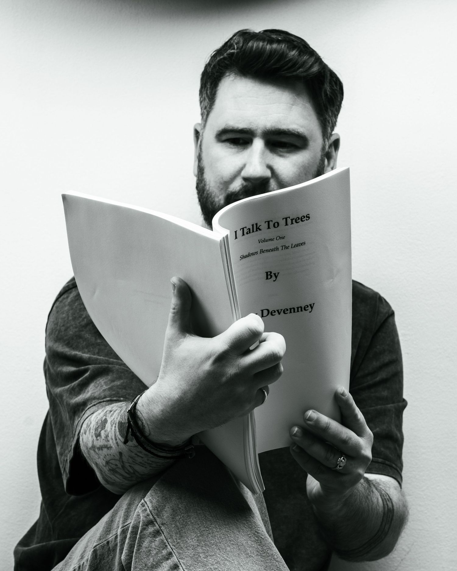 Bearded man reading a book titled I Talk To Trees by Devenney in black and white. Dave Martin Photography Studio Belfast