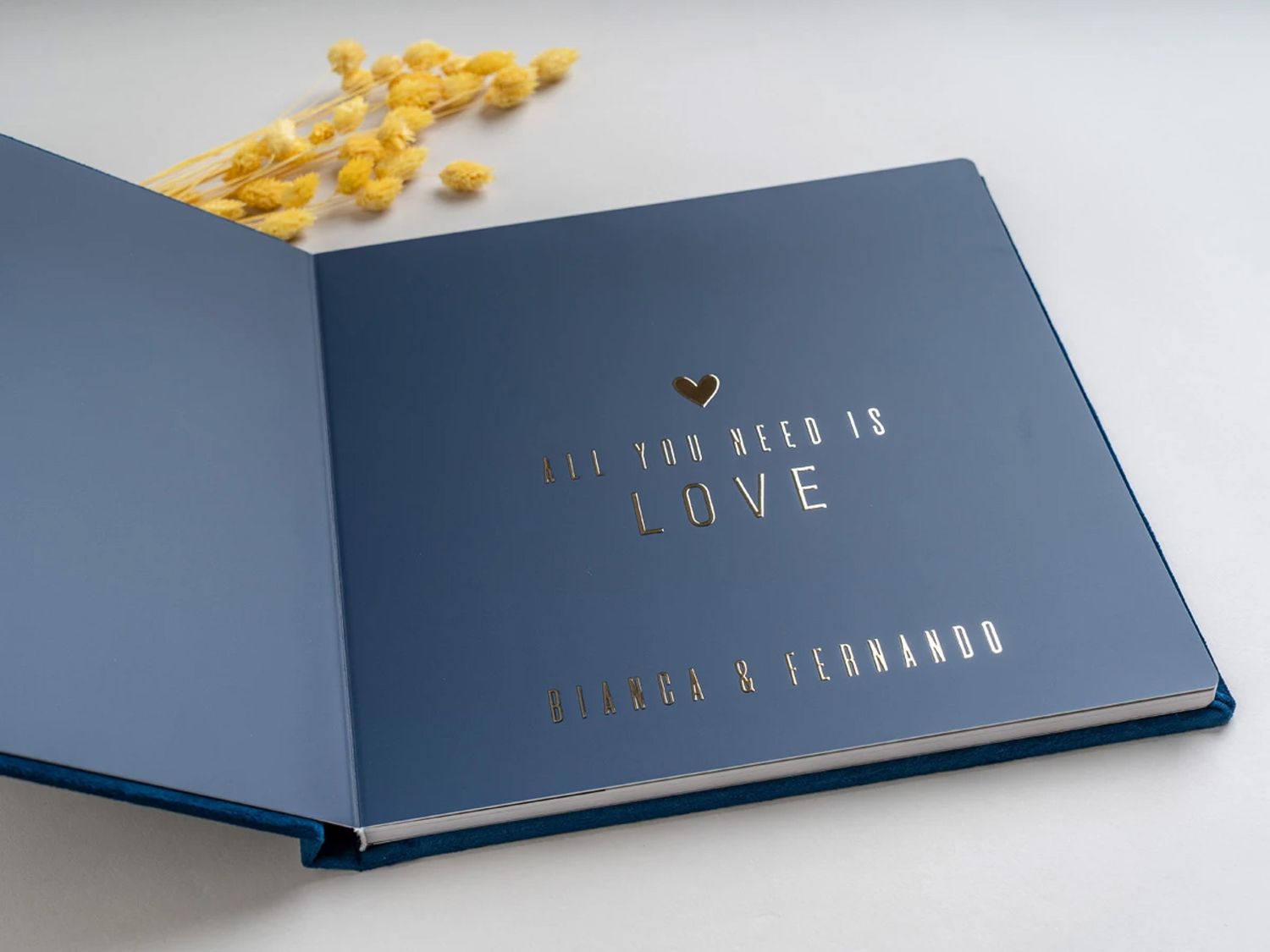 Navy blue wedding guest book with gold foil text reading All You Need Is Love, personalized with couple names Jessica and Fernando.
