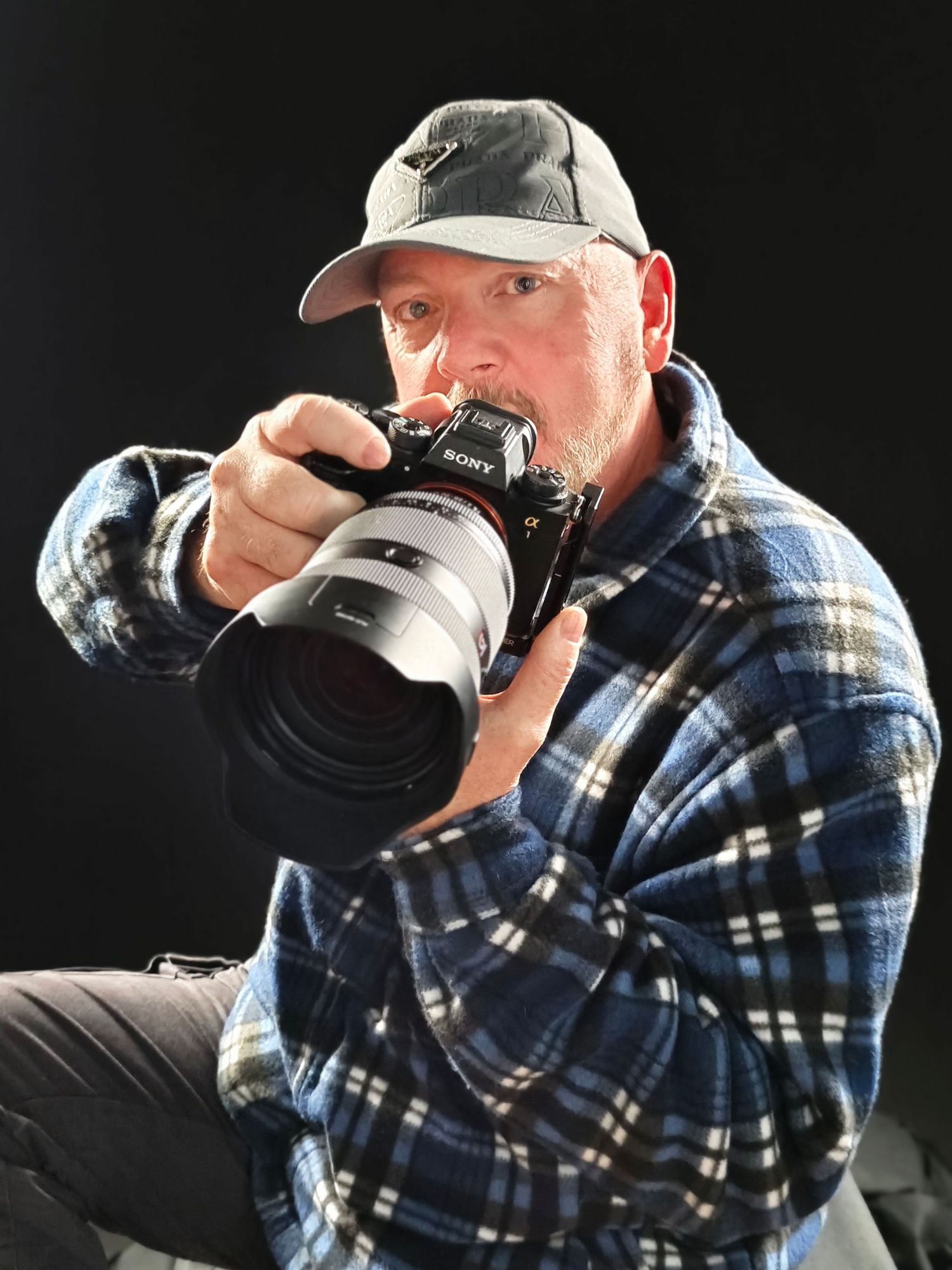 Professional photographer in plaid shirt and cap holding a Sony camera with zoom lens. Dave Martin Photographer Northern Ireland
