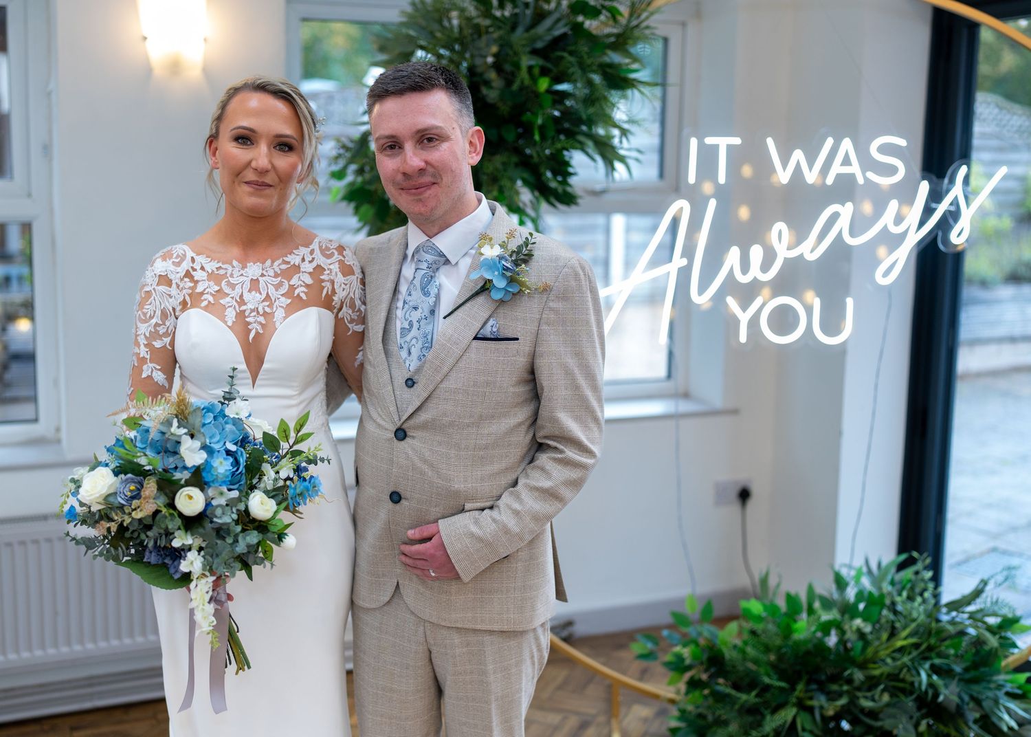 Smiling bride and groom posing with blue floral bouquet indoors. Dave Martin Photographer Northern Ireland