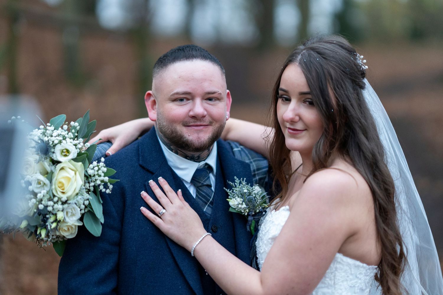 Smiling bride and groom pose together holding white floral bouquet outdoors. Dave Martin Photographer Northern Ireland