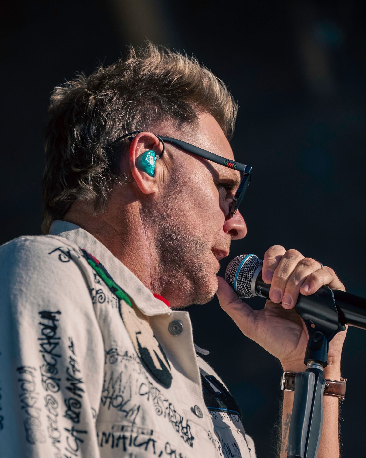Brian McFadden with glasses performing closely into microphone at outdoor concert. Dave Martin Photography Northern Ireland