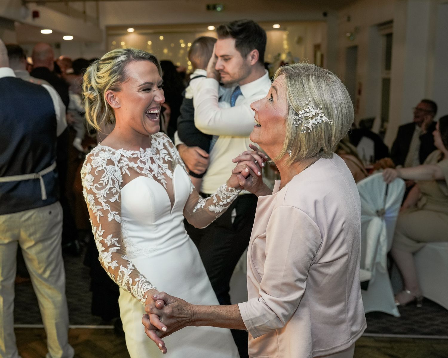 Bride in lace wedding dress laughing and dancing with guest at elegant wedding reception celebration. Dave Martin wedding Photographer NI