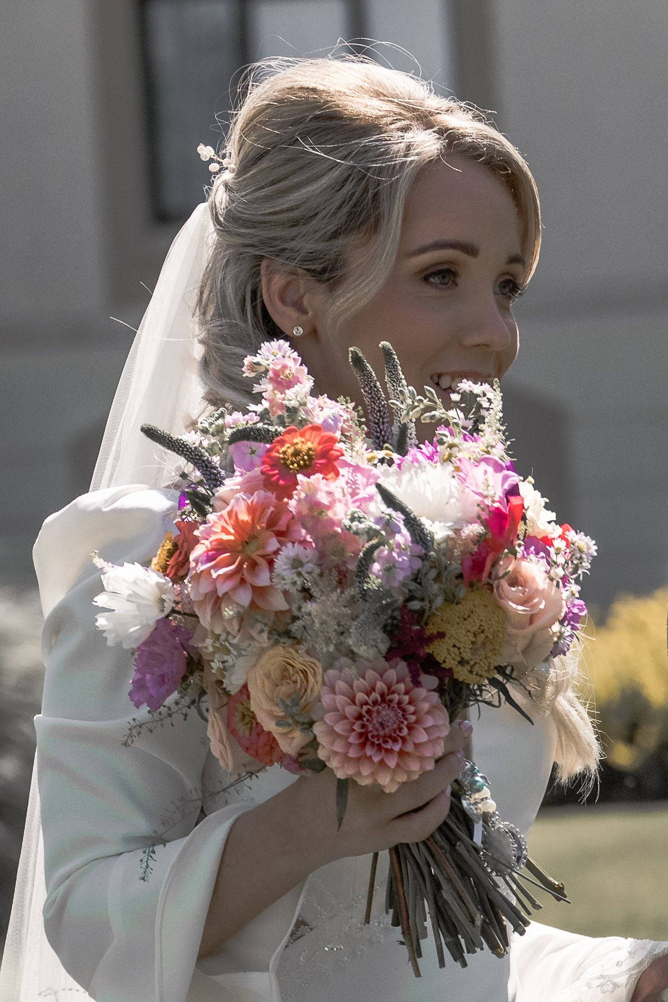 Bride in white gown and veil holding a colorful wedding bouquet of pink dahlias and mixed flowers outdoors. Dave Martin wedding Photographer