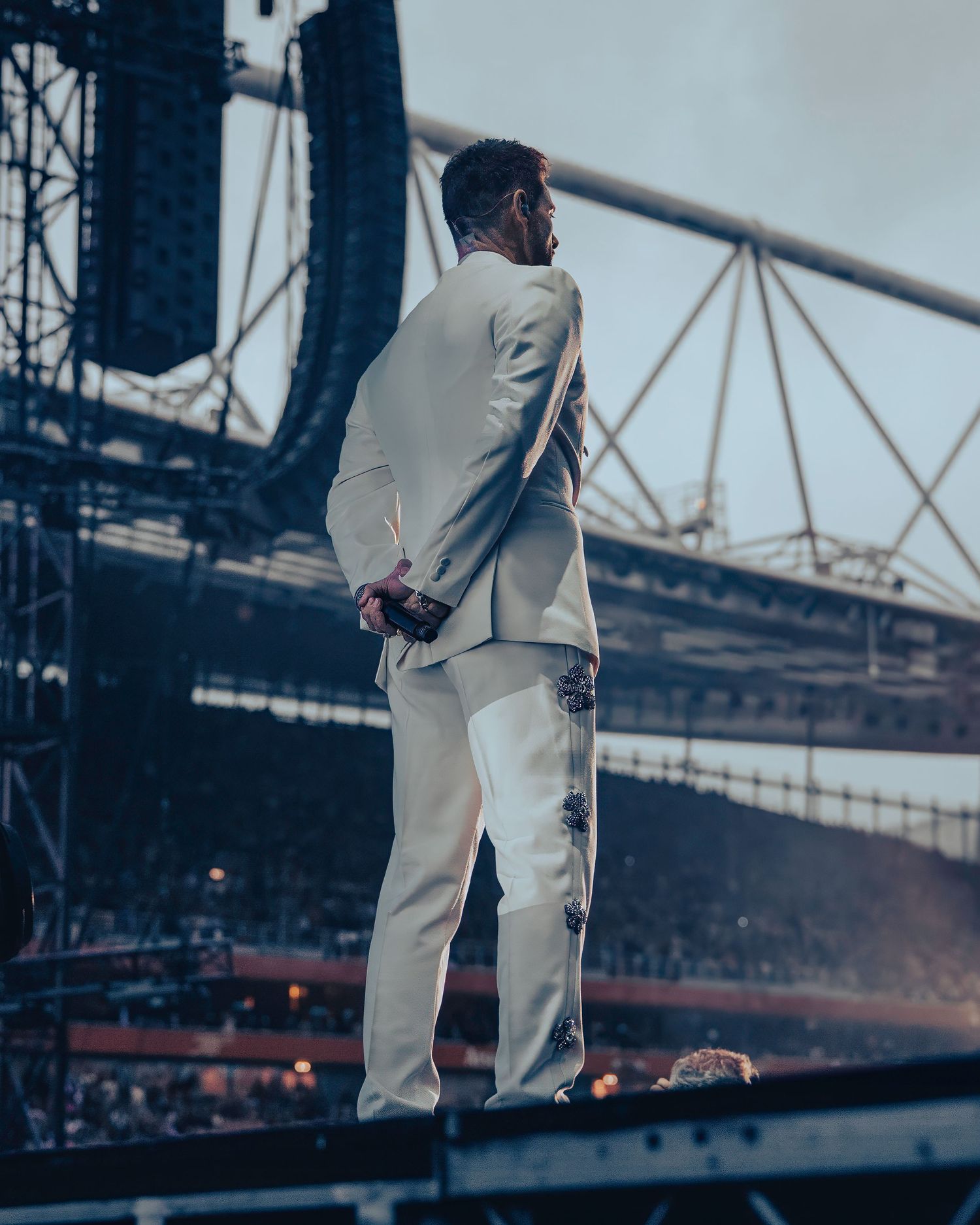 Keith Duffy in white suit stands on stage viewed from behind with large Emirates stadium structure visible. Dave Martin Photography
