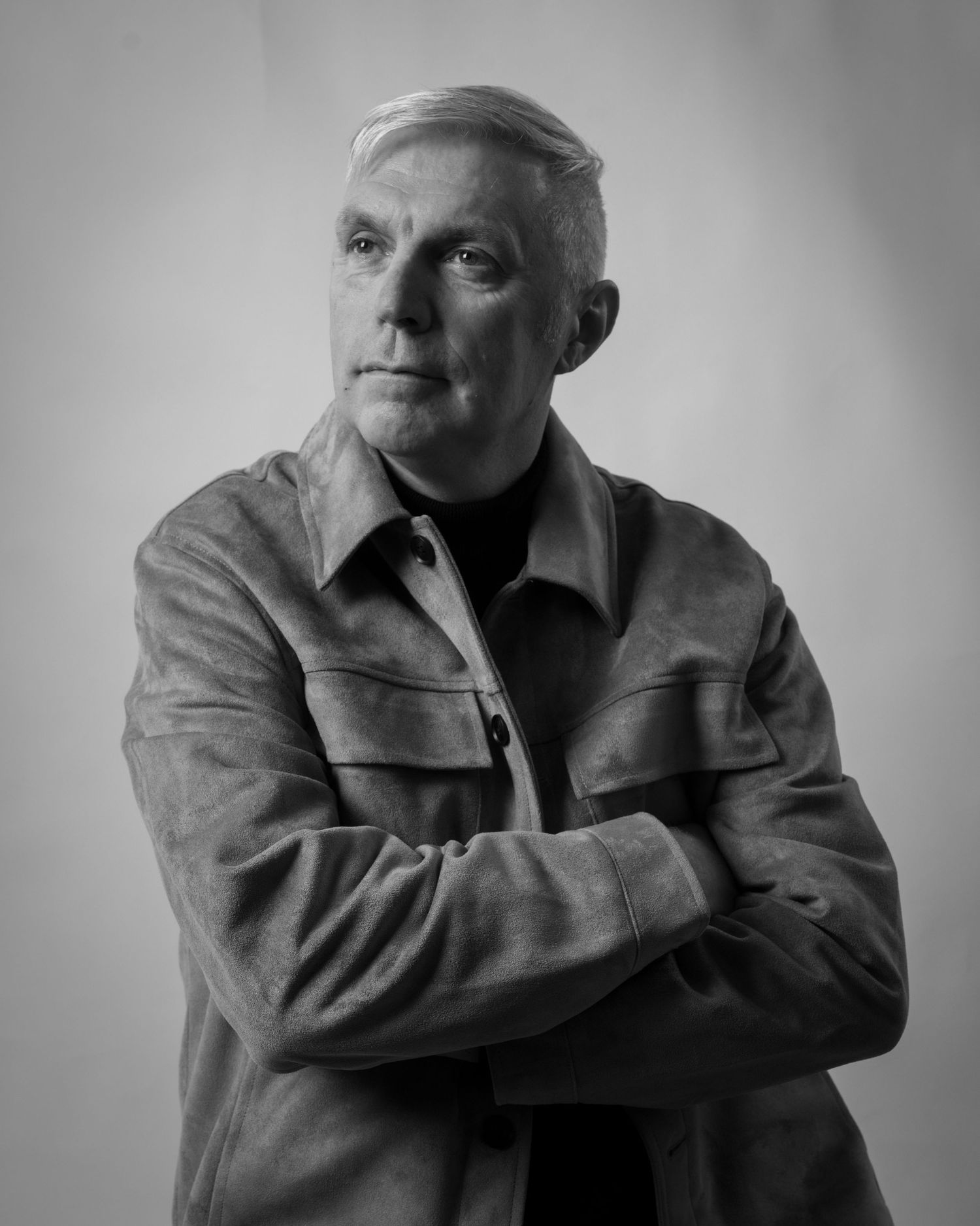 Black and white portrait of a mature man with crossed arms wearing a suede jacket, studio photography. Dave Martin Photography Studio