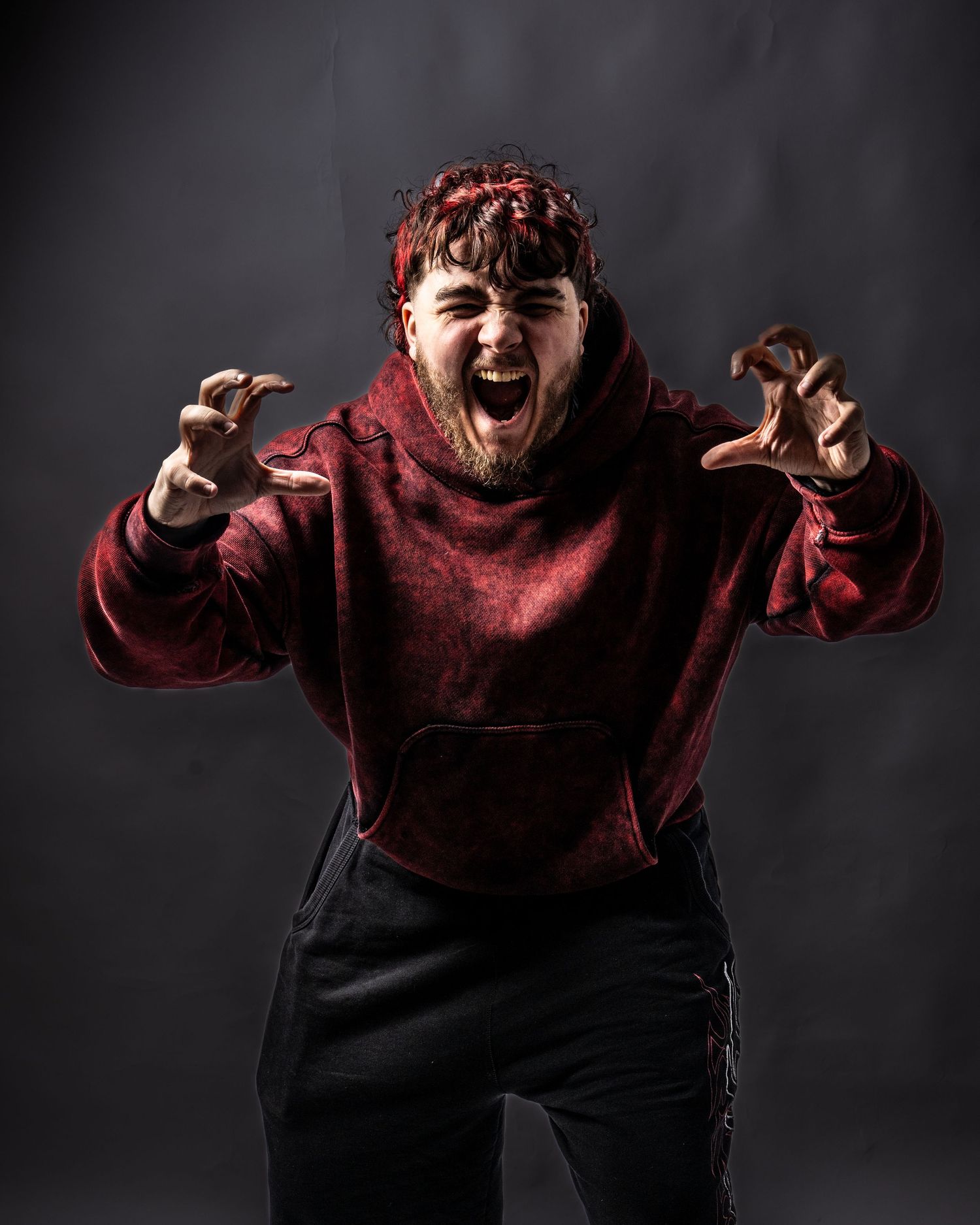 Man in red hoodie posing dramatically with clawed hands and screaming expression against dark studio background. Dave Martin Photography