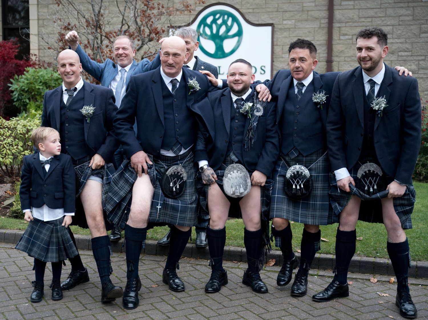 Groomsmen in traditional Scottish kilts pose playfully outside wedding venue. Dave Martin Photographer
