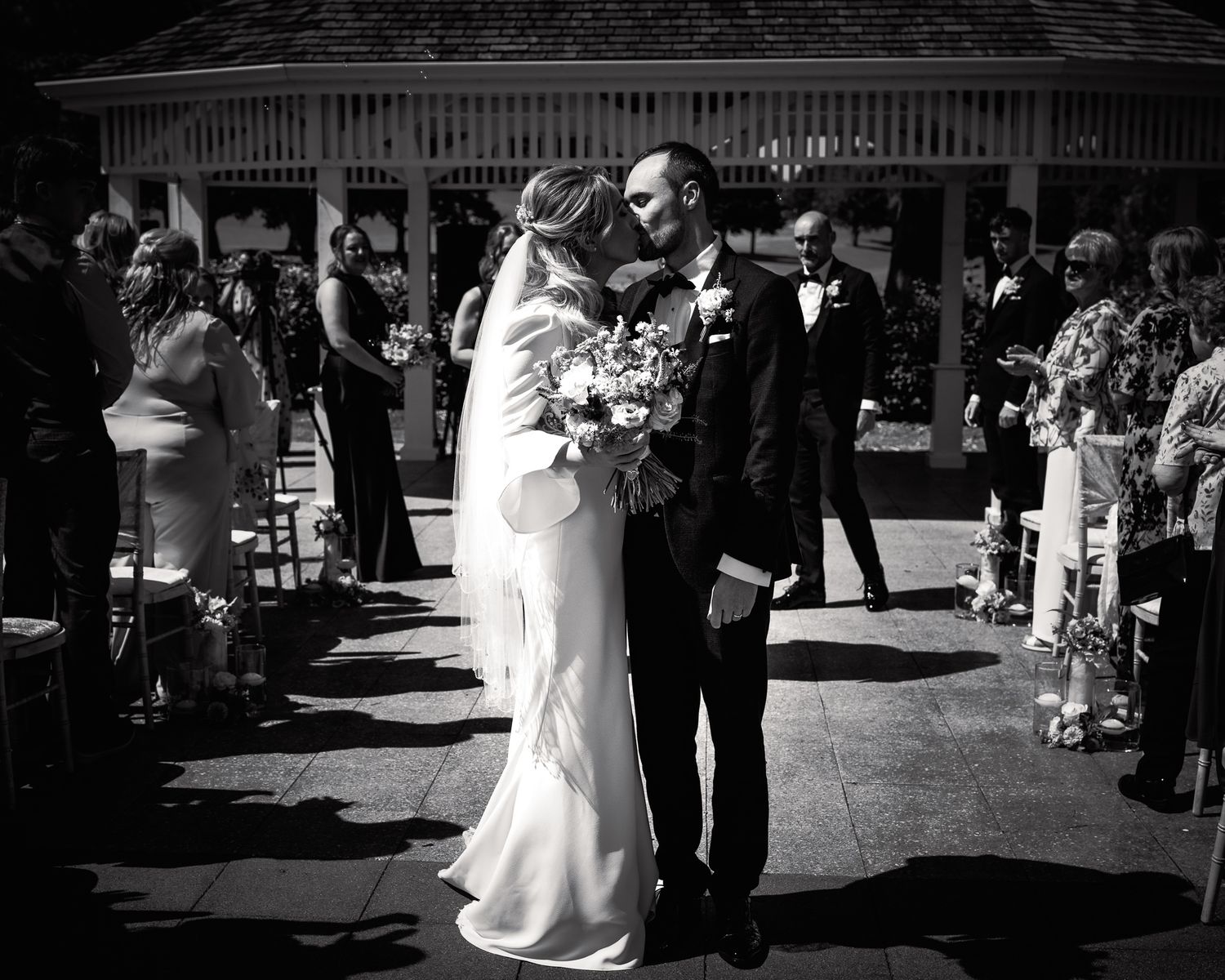 Black and white photo of a bride and groom sharing their first kiss at an outdoor wedding ceremony. Dave Martin wedding Photographer NI