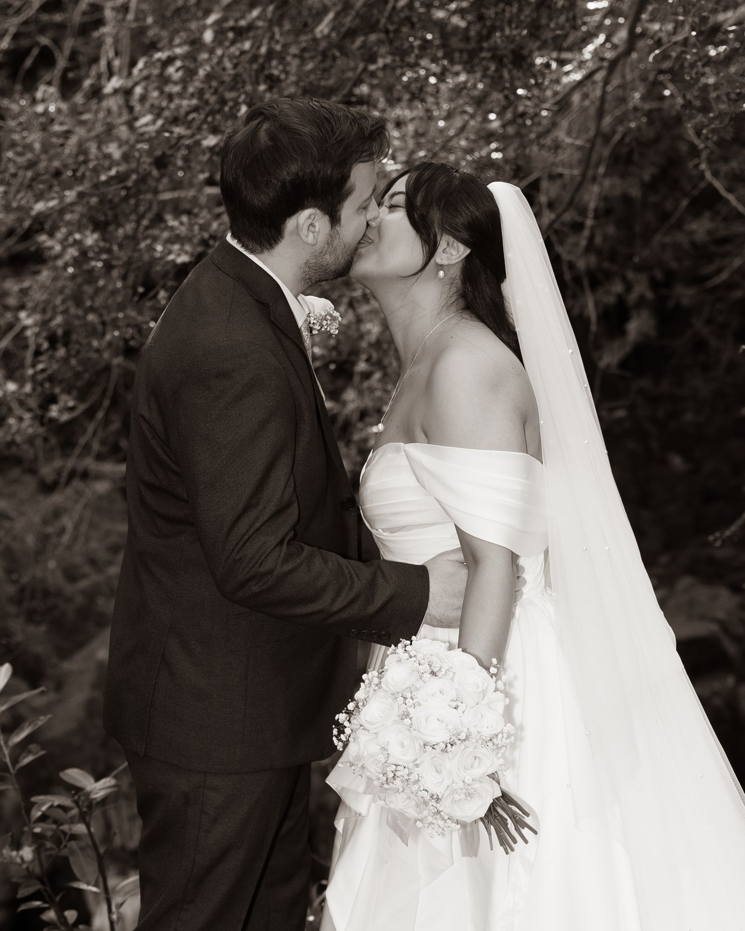 Bride and groom share first kiss in black and white photo, bride holding white bouquet outdoors. Dave Martin Photographer Northern Ireland