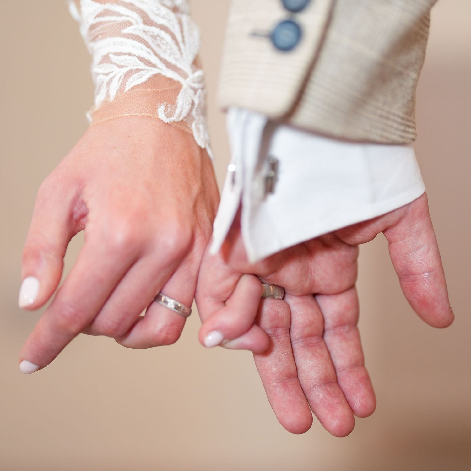 Close-up of bride and groom holding hands showing matching wedding bands, lace sleeve detail. Dave Martin Photographer Northern Ireland