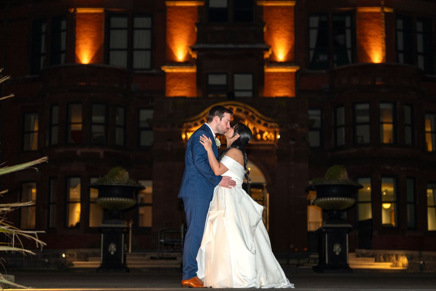 Bride and groom kiss romantically at night in front of illuminated historic building wedding venue. Dave Martin Photographer Northern Irelan