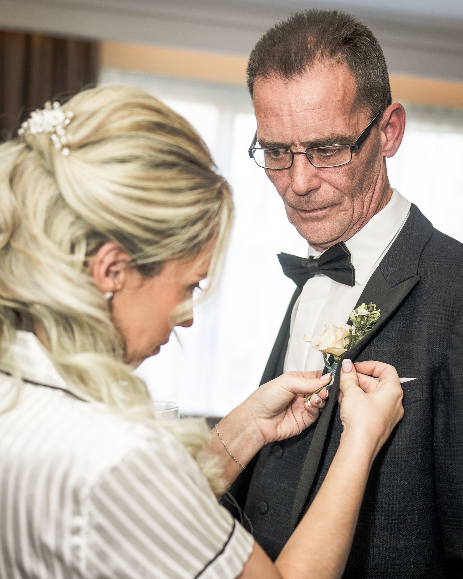 Bride pinning a boutonniere on a man in a tuxedo at a wedding ceremony preparation. Dave Martin wedding Photographer NI