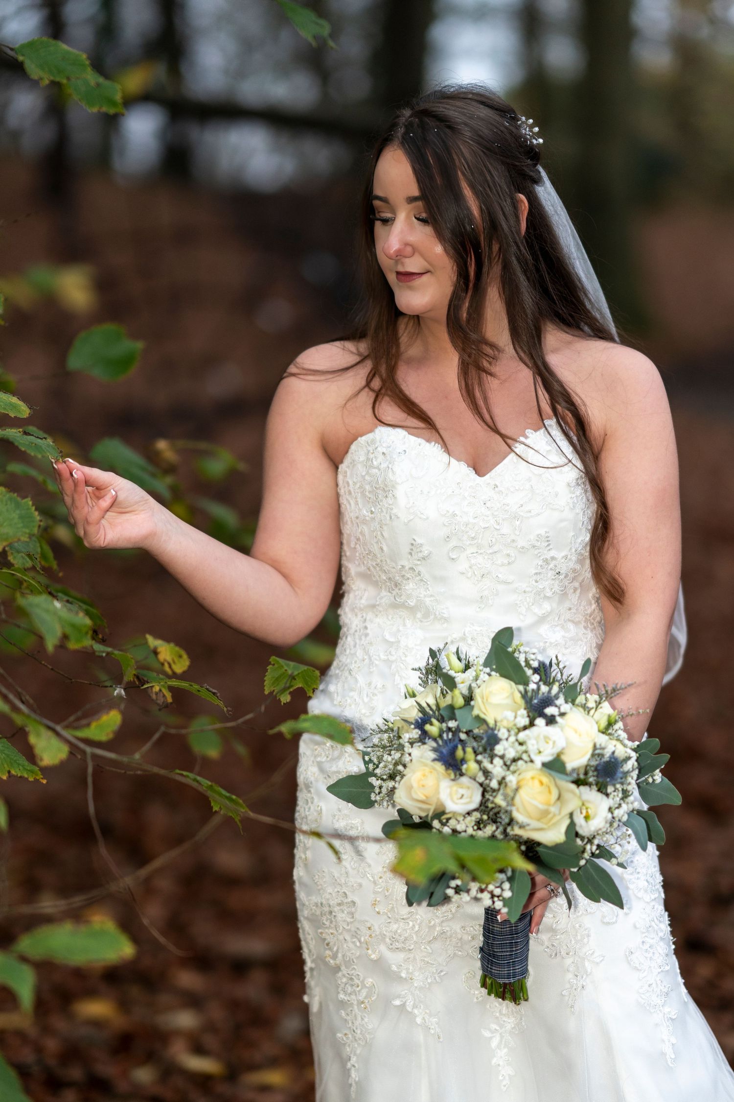 Elegant bride in lace gown holds white and blue bouquet among autumn leaves. Dave Martin Photographer Northern Ireland