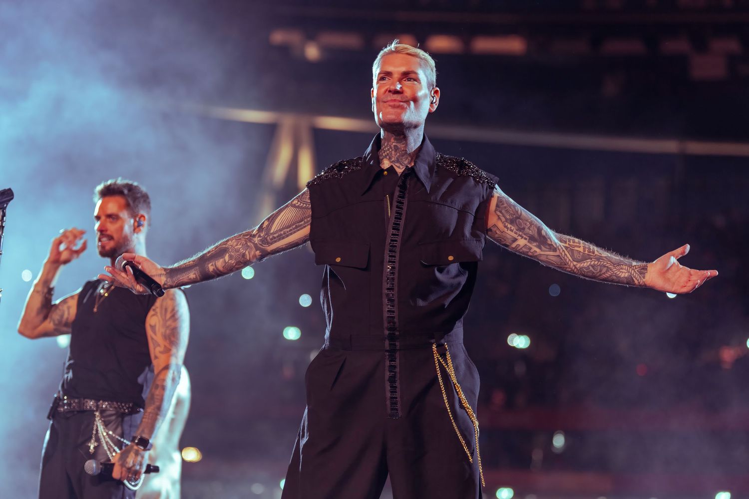 Shane Lynch Tattooed male performer in black sleeveless vest singing on stage with dramatic lighting. Dave Martin celebrity Photography