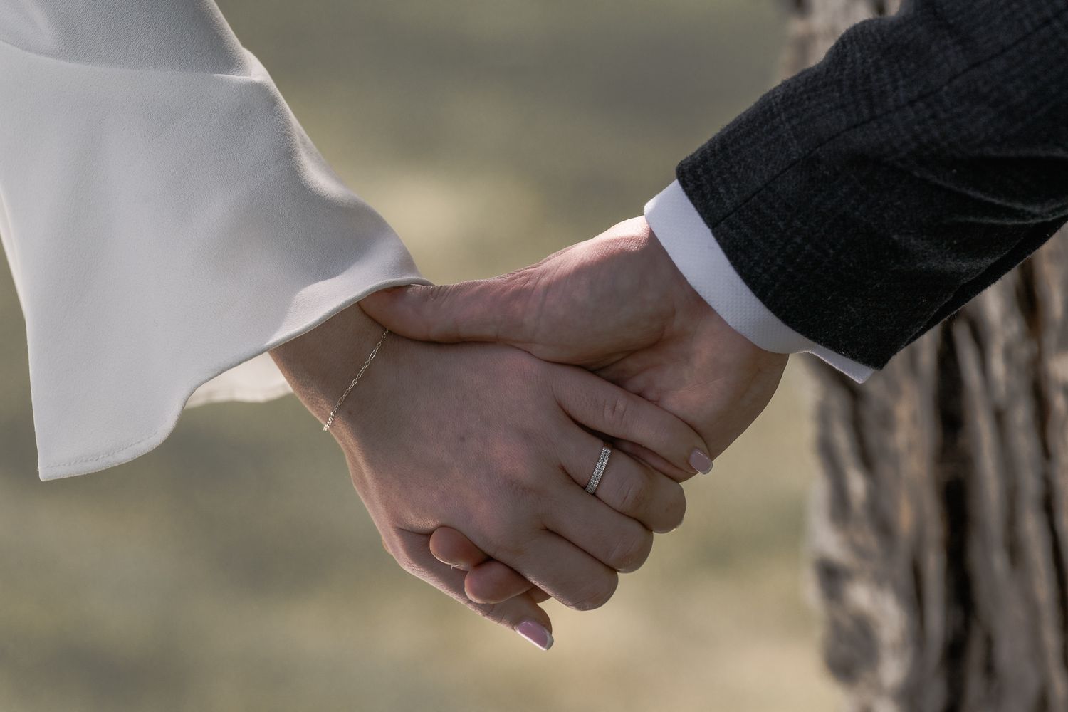 Newlywed couple holding hands, bride in white dress and groom in dark suit, both wearing wedding rings. Northern ireland weddings